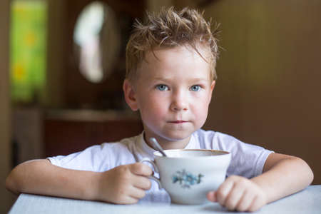 Nice little boy is drinking tea at the table at home.の写真素材