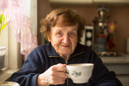 Close-up portrait of an elderly woman drinking tea at her home.