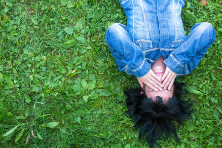 Young woman in a denim jacket lying on the grass and closes his eyes with his hands (with space for...