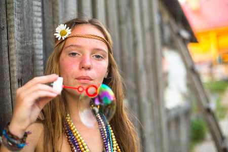 Young hippie girl blows soap bubbles on a street in the countryside.