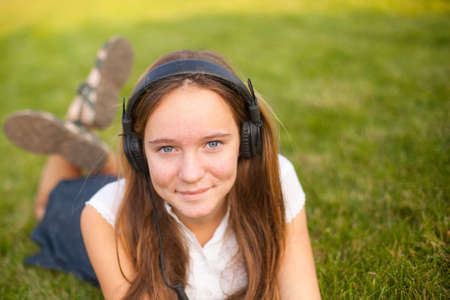 Pretty young girl in headphones enjoys music, outdoors.の写真素材