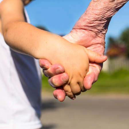 Close-up hands, grandmother holding a child hand, nature background.の写真素材