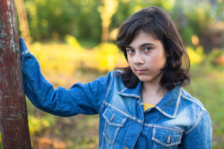 Black-haired teen girl in denim jacket portrait outdoors.の写真素材