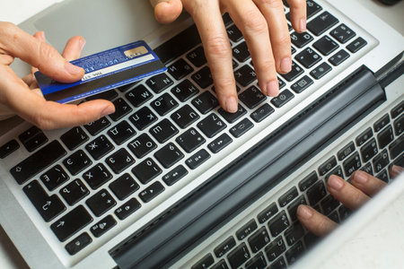 KRAKOW, POLAND - JAN 12, 2015: Female hands with bank card VISA on MacBook Pro keyboard of the computer. Editorial illustrative Shopping on internet.のeditorial素材