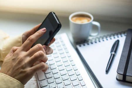 Businessman mobile phone, cup of coffe, computer keyboard and notepad in the background.の写真素材