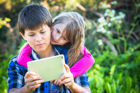 Teen boy with his younger sister sitting in a Park and using the tablet.の写真素材