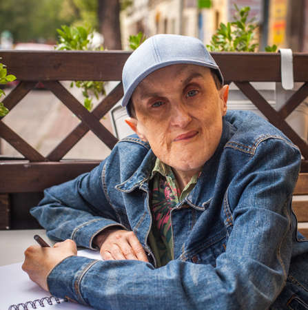 Disabled man with cerebral palsy sitting at outdoor cafe with a notebook and pencil.の写真素材