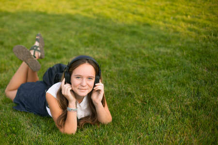 Young cute girl enjoying music with headphones while lying in the grass. With space for text.の写真素材