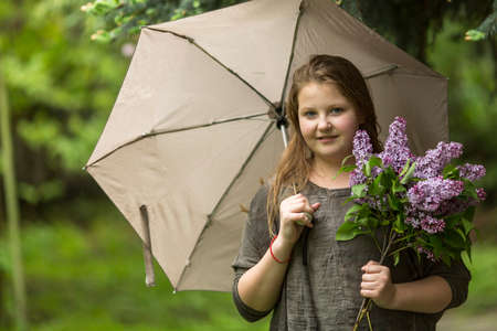 Portrait of teen girl with an umbrella and a bouquet of lilacs.の写真素材