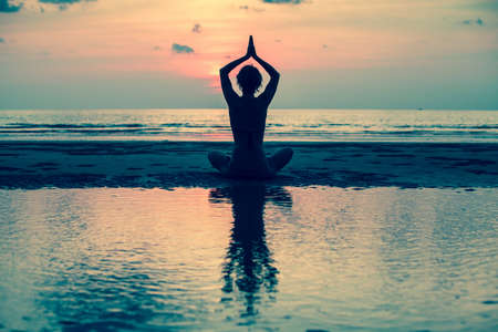 Yoga, silhouette young woman on the beach at sunset, harmony of health.の写真素材