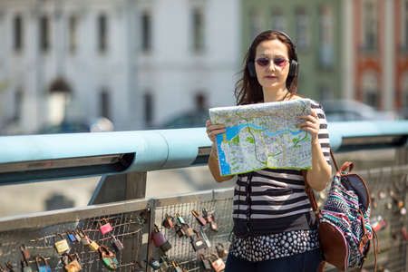 Young female tourist, standing on the pedestrian bridge with locks of love, with map looking for the direction.の写真素材