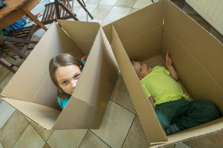 Children sit in cardboard boxes. Unpacking boxes and moving into a new home. Housewarming concept.の写真素材