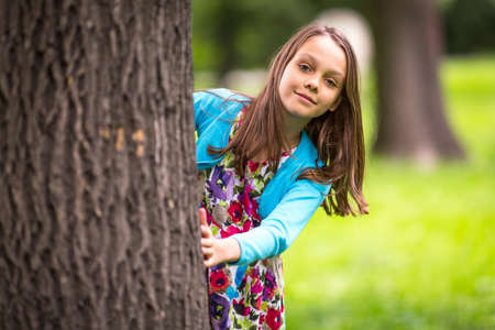 Cute little girl peeking from behind a tree.の写真素材
