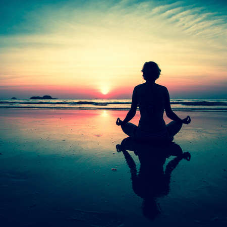 Silhouette young woman practicing yoga on the beach at surrealistic sunset.の写真素材