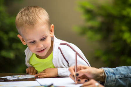 Little boy learning to draw with a pencil and with interest the hands of an adult.の写真素材