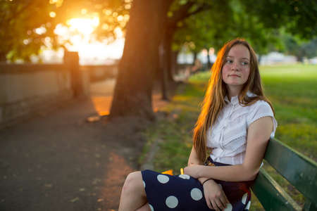 Beautiful young long haired girl sitting in a Park during golden sunset.の写真素材
