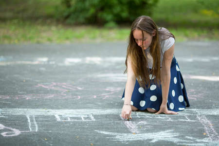 Lovely teen girl draws with chalk on the pavement.の写真素材