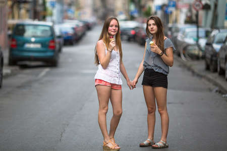 Two teen girls with ice cream stand on the street holding hands.の写真素材