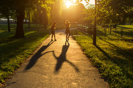 Silhouettes of two girls walking down the alley holding hands, during amazing sunset.の写真素材