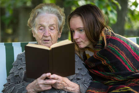 An elderly woman reading a book sitting in the garden with his granddaughter.の写真素材