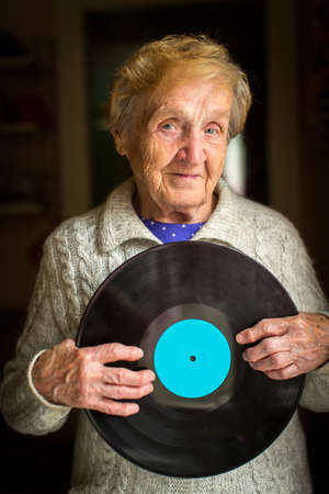 Old woman stands in the house holding the vinyl record in his hands.の写真素材