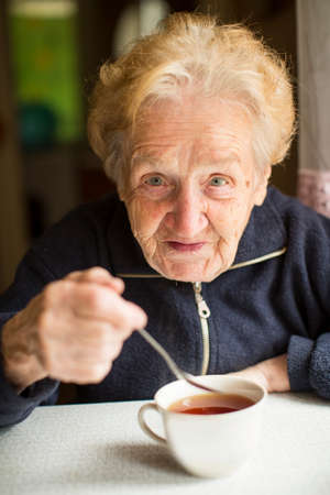 Grandmother sitting at the table drinking tea from a Cup.の写真素材