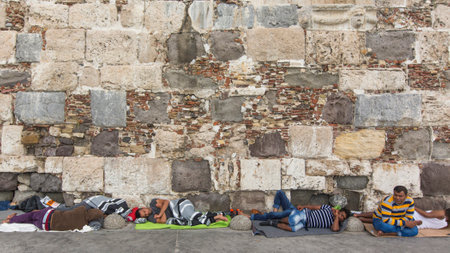 KOS, GREECE - SEP 27, 2015: War refugee sleeping on the ground along the stone wall. Kos island is located just 4 kilometers from the Turkish coast, and many refugees come from Turkey in an inflatable boats.のeditorial素材