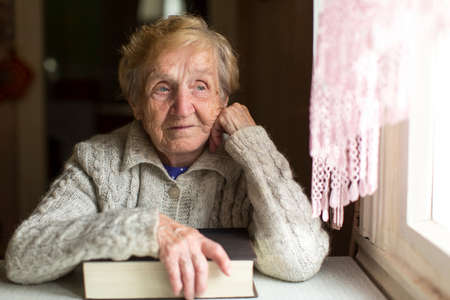 An elderly woman with a book sitting near the window.の写真素材