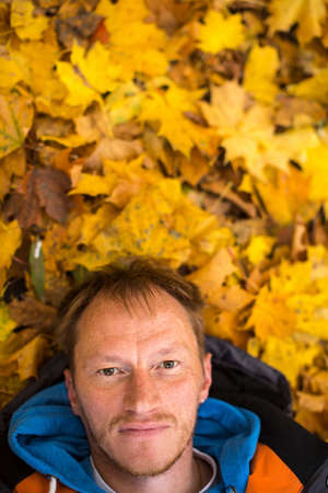 Portrait of a young man lying on yellow autumn leaves.の写真素材