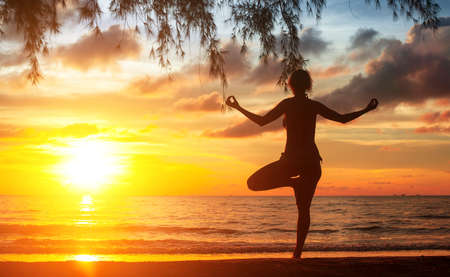 Young woman practicing yoga at sunset on the Ocean coast.の写真素材