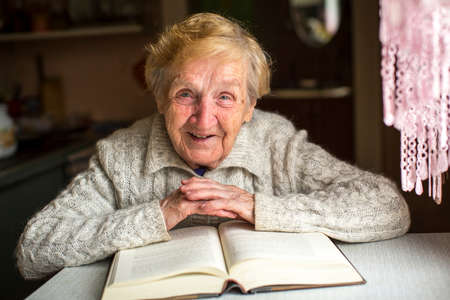 An elderly woman sits with a book at the table.の写真素材