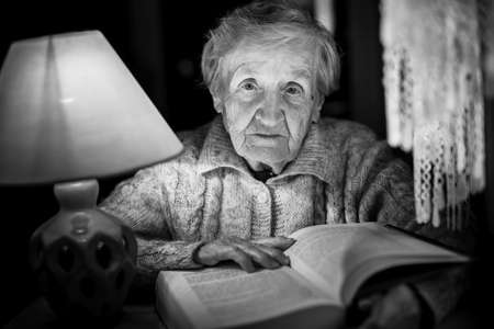 An elderly woman reading a book with night lamp. Black and white photo.の写真素材
