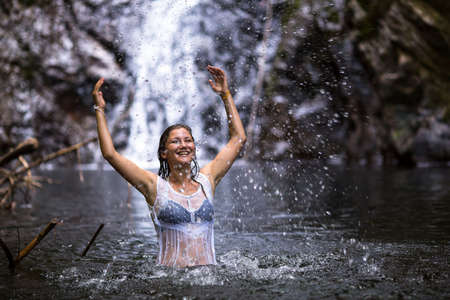 Young beautiful woman bathing in a forest pond near the waterfall.の写真素材