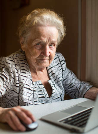 An elderly woman sitting with laptop.