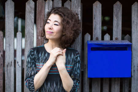 Beautiful young asian woman stands near the fence with a mailbox.の写真素材
