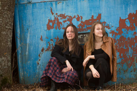 Teen girls sitting on a background of old iron wall.の写真素材