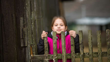 Cute little girl behind a wooden fence in the village.の写真素材