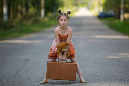 Cute little girl with suitcase and Teddy bear is on the road.の写真素材