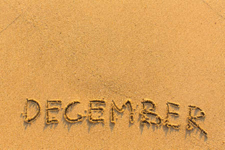December - word inscription on the gold sand sea beach.