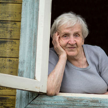 Portrait of a Slavic grandmother looking out the window of his house.の写真素材