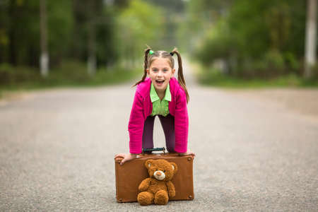 Little traveller girl on the road with a suitcase and a Teddy bear.の写真素材