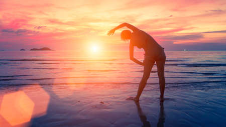 Female silhouette performs physical exercises on the beach after sunset.の写真素材