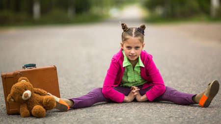 Little girl traveller on the road with a suitcase and a Teddy bear.の写真素材