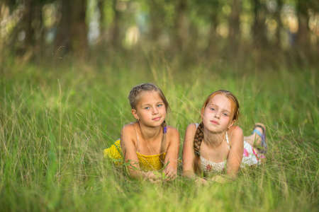 Two little sisters lying in the meadow looking at the camera.の写真素材