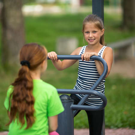 Kids girls practice gymnastics on the public sport equipment outdoors.