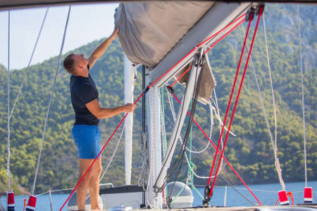 Yachtsman pulls the rope controlling the sail on sailing boat.