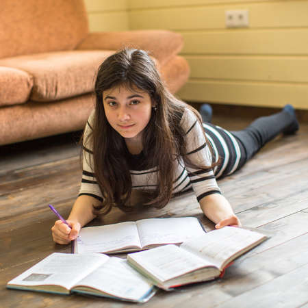 Schoolgirl doing homework lying on the floor in the room.