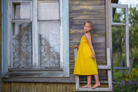 Little girl in a yellow dress standing on a wooden ladder near the farmhouse.の写真素材