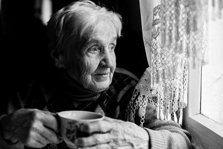 Elderly woman drinking tea looking out the window. Black-and-white photo of high contrast.の写真素材
