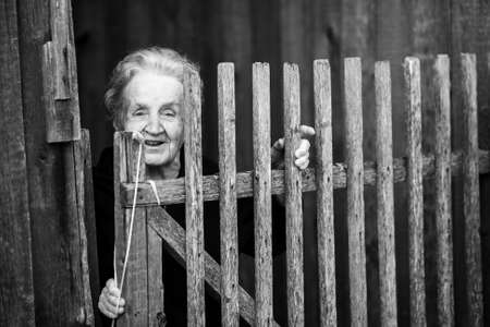 An elderly woman near the wooden fence. Black-and-white photo.の写真素材